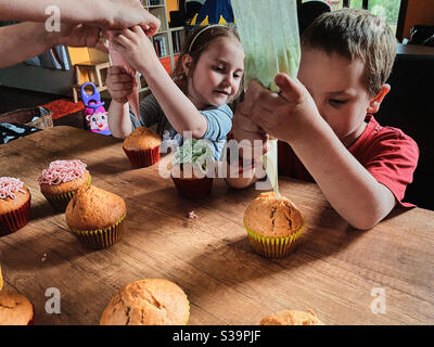 Gruppe von Kindern backen Cupcakes, Quetschen Sahne aus Süßwarenbeutel, Zutaten vorbereiten, Belag, Streuseln für die Dekoration von Cookies. Kinder kochen, arbeiten zusammen in der Küche zu Hause Stockfoto