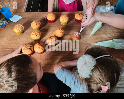 Gruppe von Kindern backen Cupcakes, Quetschen Sahne aus Süßwarenbeutel, Zutaten vorbereiten, Belag, Streuseln für die Dekoration von Cookies. Kinder kochen, arbeiten zusammen in der Küche zu Hause Stockfoto