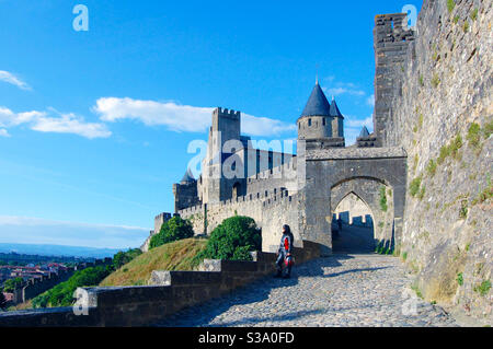 Schloss von Carcassonne in der Provence, Frankreich, Blick auf das Schloss von einer der Zufahrtsstraßen Kopfsteinpflaster Blick auf den Eingang, blauer Himmel in einem sonnigen Frühlingstag, moderne Lichter Stockfoto