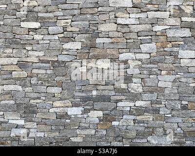 Wand aus seltsam geformten, grauen und anderen erdfarbenen Ziegeln aus Stein, Schaffung abstrakter Hintergrundtextur geeignet für Compositing Stockfoto