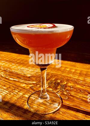 Martini-Cocktail für Weihnachtsstimmung - mit einem Schaumtop Und Passionsfrucht in einem langstieligen Glas auf einem Holztisch Stockfoto