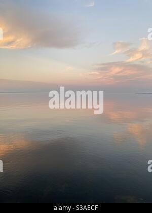 Sanfter, pastellfarbener Sonnenuntergang am ruhigen, noch in der Bucht abgehenden Wasser Stockfoto