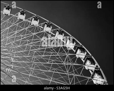 Blick auf eine Fahrt mit dem Riesenrad auf einem unterhaltsamen Jahrmarkt. Strahlender Sonnenschein bedeutet einen dunklen Himmel?! Bildnachweis - ©️ COLIN HOSKINS. Stockfoto