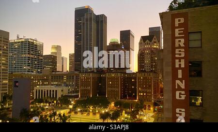 LOS ANGELES, CA, JUL 2020: Blick auf das Millennium Biltmore über Pershing Square mit Wolkenkratzern und anderen hohen Gebäuden dahinter. Pershing Square Building im Vordergrund. Abenddämmerung Stockfoto