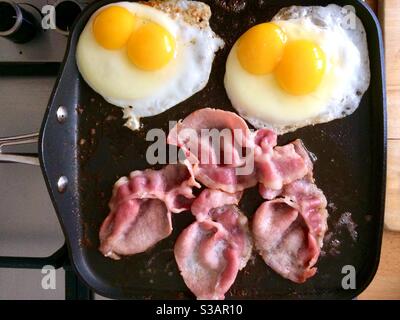 Spiegeleier mit Doppelpasse und Speck auf einer Grillplatte. Stockfoto