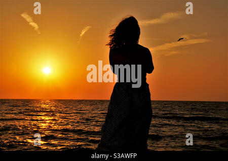 Silhouette einer jungen Frau am Meer bei Sonnenuntergang Stockfoto