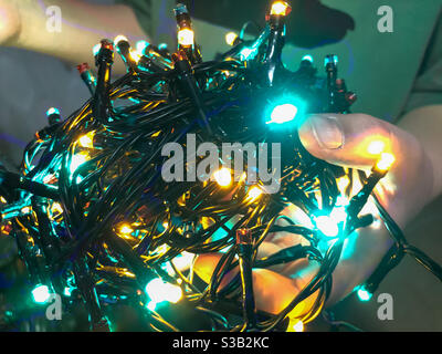 Ein Kind hält Lichterketten bereit, an einem Weihnachtsbaum zu hängen. Stockfoto