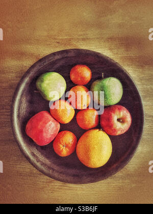 Ein Blick von oben auf eine hölzerne Obstschale mit Orangen, Äpfeln und Mandarinen. Gesunde Früchte sind unschlagbar. 5 pro Tag und all das?! Bildnachweis ©️ COLIN HOSKINS. Stockfoto