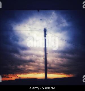 Ein Foto aus dem Fenster an einem grauen und stürmischen Tag, mit einem Telegrafenmast und Drähten im Vordergrund. Düsterer brodelender Himmel. Stockfoto