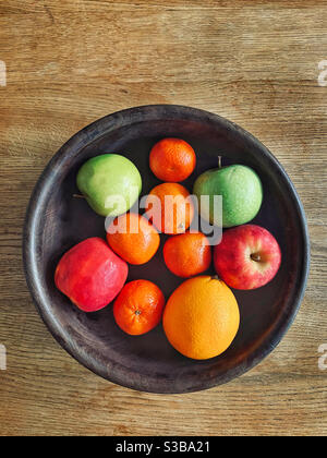 Ein Blick von oben auf eine hölzerne Obstschale mit Äpfeln, Mandarinen und einer Orange. Viele gesunde Lebensmittel inc. Vitamin C. Foto ©️ COLIN HOSKINS. Stockfoto