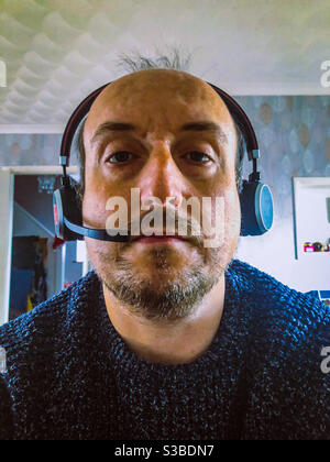 Mann mittleren Alters, der von zu Hause aus mit einem Computer-Headset bei einem Konferenzgespräch arbeitet. Stockfoto