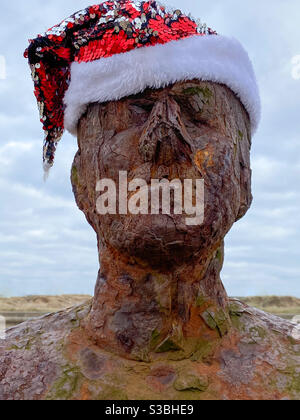 Einer der hundert eisernen Männer von Anthony Gormley's Another Place echte Live-Größe Skulpturen, Statuen auf Crosby Strand trägt einen festlichen Weihnachtshut Stockfoto