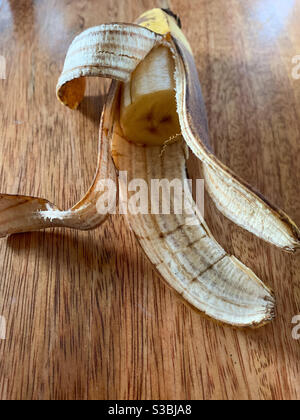Eine halbe Banane in ihrer Schale auf einem Holztisch Stockfoto