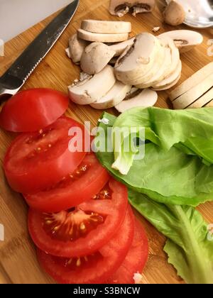 Gesunde Zutaten für einen Salat alle auf einem Holzschneidebrett in einer Wohnküche zusammen mit einem Schälmesser geschnitten, USA Stockfoto