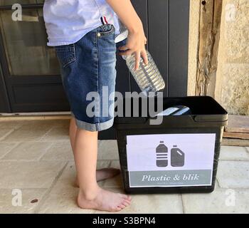 Kleiner Junge, der eine Plastikflasche in den Recyclingbehälter legt Zu Hause Stockfoto