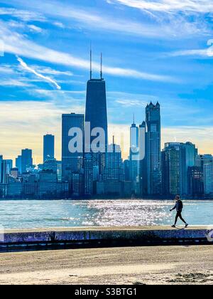 Mann, der entlang der Meeresmauer am North Avenue Beach mit der Skyline von Chicago im Hintergrund läuft. Stockfoto