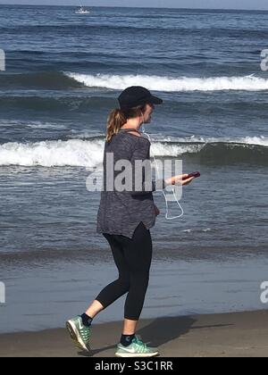 Frau, die am Meer entlang geht und mit ihrem Handy spricht Stockfoto