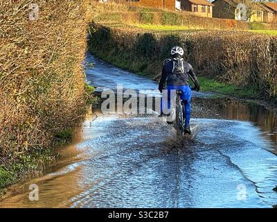 Menschen, die durch Hochwasser auf einer schmalen Landstraße radeln Stockfoto