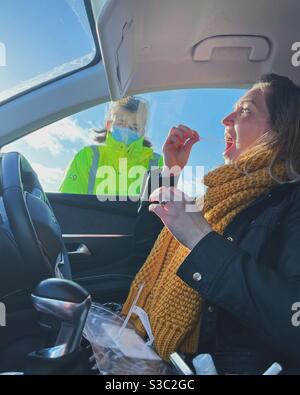 Frau im Auto, die bei der Fahrt durch die COVID-19-Testanlage beaufsichtigt wird. Stockfoto