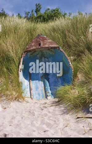 Altes Segelboot halb in den Sand getaucht in der Dünen am Strand auf den Isles of Scilly in Sommer unter hohen wilden Seegräser auf einem hellen warmen Sommertag Stockfoto