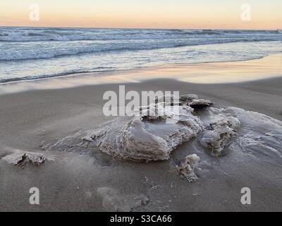 Winterwellen hinterlassen eisige Sandskulpturen am Lake Michigan Beach. Sonnenuntergang am Gillson Beach am Ufer des Sees in Illinois. Stockfoto