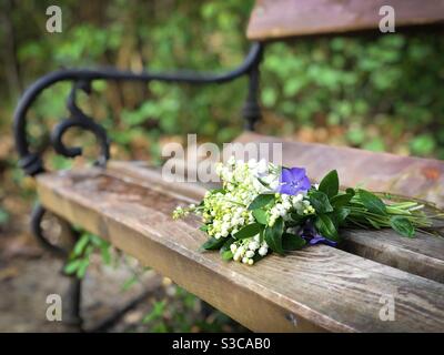 Frühlingsstrauß aus lila Blüten und Lilien der Tal auf einer Holzbank platziert Stockfoto