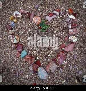 Bunte Herzform aus Strandkieseln auf Sand Stockfoto