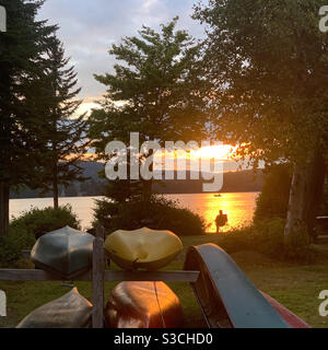 Kanus mit Blick auf den Back Lake und ein Mann, der den Sonnenuntergang in der Tall Timber Lodge, Pittsburg, New Hampshire, USA, beobachtet Stockfoto