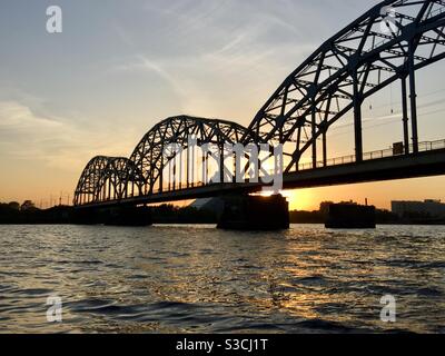 Eine Brücke über dem Fluss Daugava (Riga, Lettland) mit Sonnenuntergang im Hintergrund Stockfoto