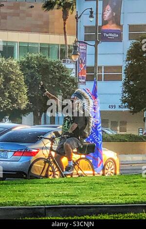 In Los Angeles ist es nicht ungewöhnlich, einen Mann in einem T-Shirt, Shorts und einem indischen Kopfschmuck zu sehen, der mitten im Verkehr in Beverly Hills Fahrrad fährt und eine Flagge trägt Stockfoto