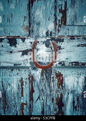 Altes rustikales Hufeisen an der Holztür mit blau abblätternder Farbe Stockfoto