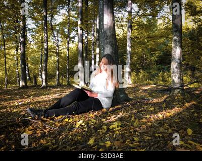 Frau, die im Herbst unter einem Baum liest Stockfoto