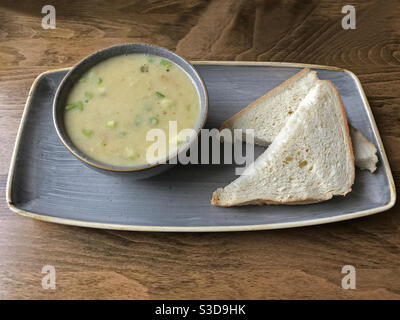 Eine handwerkliche Gemüsesuppe mit Süßkartoffeln, Lauch, Apfel und Sellerie wird neben zwei Scheiben Weißbrot gezeigt, die in einem Café auf einem Tisch plattiert sind. Stockfoto