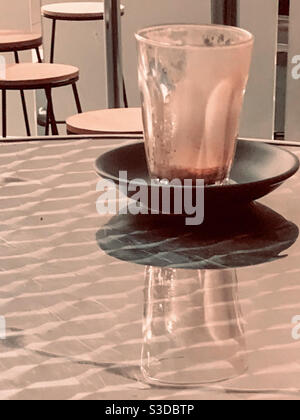 Übrig gebliebene Latte-Tasse, Reflexion eines Morgenkaffees, Glas und Untertassen auf einem glänzenden Tisch, Glas leer Stockfoto