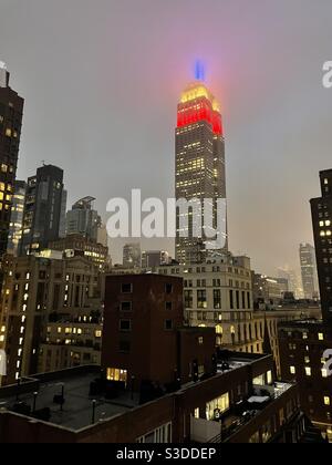 Die Lichter auf dem Empire State Building, entworfen von Marc Brickman, leuchten rot-weiß und blau gegen den Abendhimmel und durch einen nebligen Nebel in New York City, USA Stockfoto
