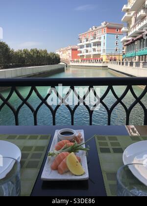 Sushi Lunch auf einer Restaurantterrasse mit Blick auf die bunten Gebäude des Qanat Quartiers auf der künstlichen Insel der Perle in Doha, Katar Stockfoto