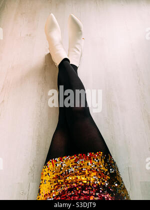 Frau saß auf dem Boden in einem Paillettenkleid und Weiße Stiefeletten Stockfoto