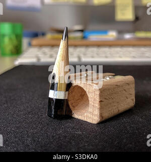 Ein winziger Bleistift mit Bleistiftspitzer, auf einem Schreibtisch mit Computer im Hintergrund. Stockfoto