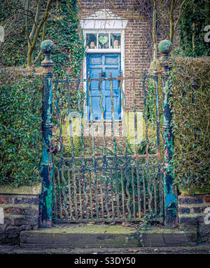 Altes schmiedeeisernes Tor mit schuppigen Schichten farbiger Farbe Und Haus im Hintergrund mit blauer Tür Stockfoto