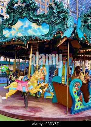 Eine dunkelhaarige Frau reitet auf dem farbenprächtigen verzierten Karussell im Bryant Park, Manhattan, New York, USA Stockfoto