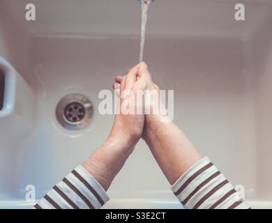Sicht auf ein Paar Hände, die sich darunter waschen Ein fließendes Leitungswasser und fließendes Wasser über einem Waschbecken mit Steckbohrung Stockfoto