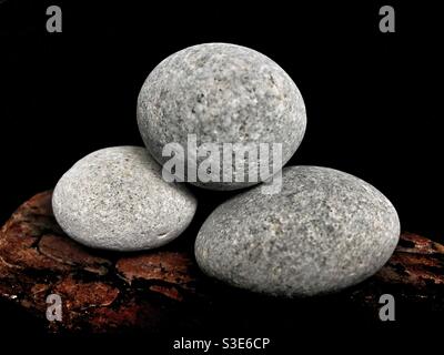 Drei runde Steine auf einem Holzstück Auf schwarzem Hintergrund Stockfoto