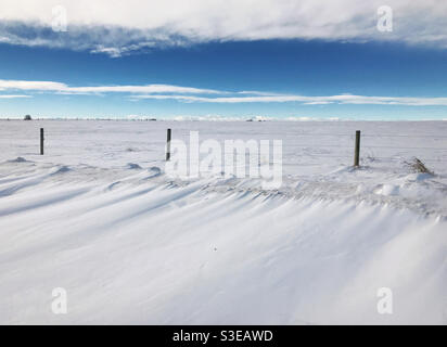 Schneeverwehungen und schneebedeckte Felder, mit Wolken und blauem Himmel. Prärien in Alberta, in der Nähe von Calgary, Kanada. Stockfoto