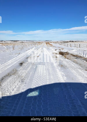 Der Schatten eines Fahrzeugs, das eine Kehrtwende macht, nachdem es auf einer unbefestigten Straße in der Prärie tiefen Schnee erreicht hat. In Der Nähe Von Calgary, Alberta, Kanada. Stockfoto