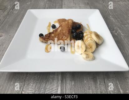 Zimt French Toast serviert mit Banane und Heidelbeeren in Scheiben geschnitten und Garniert mit Ahornsirup Stockfoto