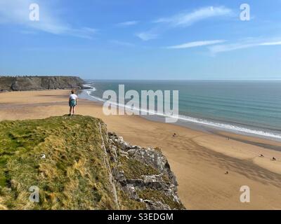 Junge Frau auf einer Klippe mit Blick auf Three Cliffs Bay, Gower, South Wales, Ebbe. Stockfoto