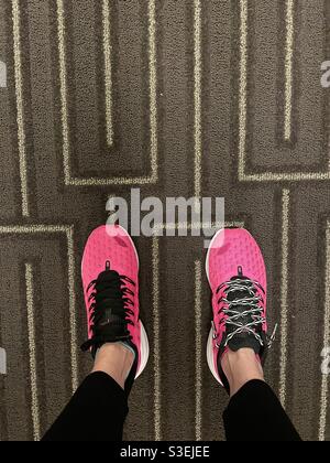 Damen Paar heiße pinke Nike Sportschuhe mit nicht übereinstimmenden Schnürsenkel auf einem Teppich Stockfoto