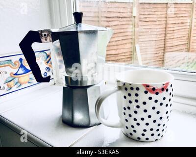 Eine Tasse Kaffee mit einem roten Lippenstift als nächstes Zu einem Moka-Topf aus Metall Stockfoto