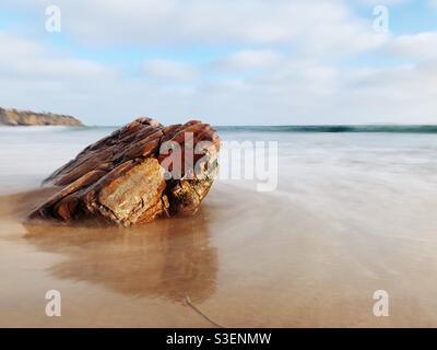 Lange Aufnahme von Felsen am Sandstrand mit Wasser aus dem Meer. Stockfoto