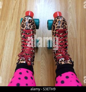 POV-Aufnahme der Füße einer Frau in Rollschuhe mit Leopardendruck und in Leggings mit rosa und schwarz gepunkteten Tierdrucken Stockfoto